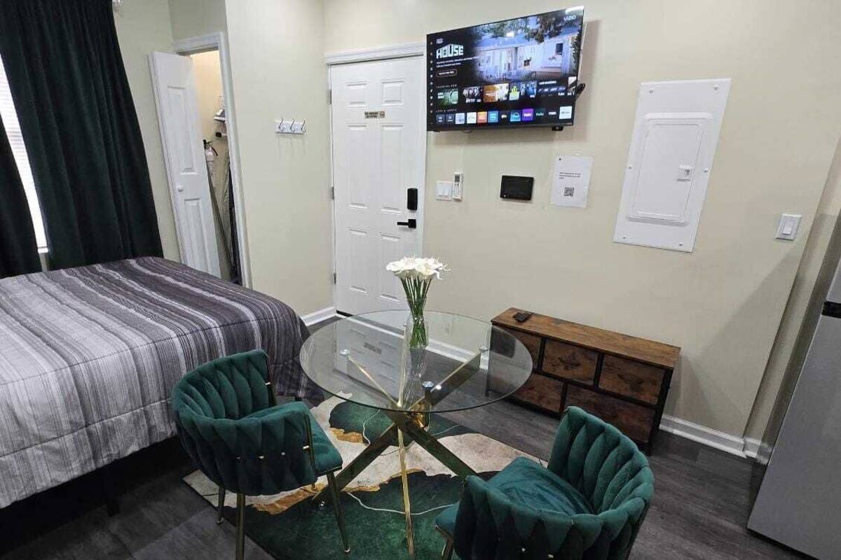 Hotellihuoneessa on sänky, lasipintainen pöytä tuoleineen, seinälle asennettu televisio ja puinen kaappi.