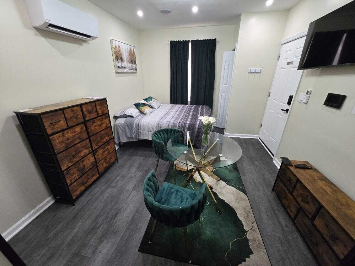 A compact hotel room with a bed, a dresser, a TV, and a small dining table with chairs.