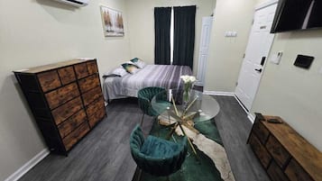 A compact hotel room with a bed, a dresser, a TV, and a small dining table with chairs.