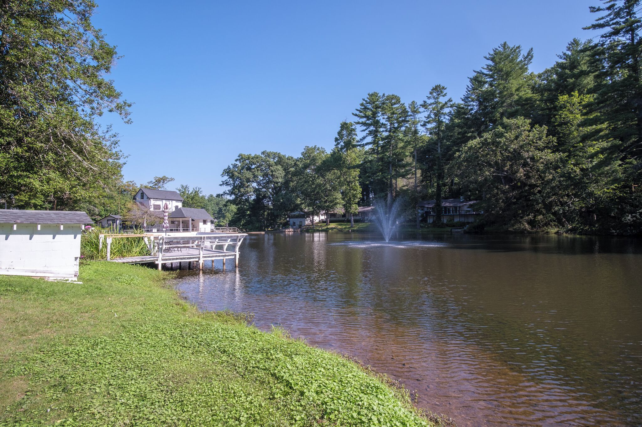 A calm lake with a fountain, surrounded by trees and a dock.