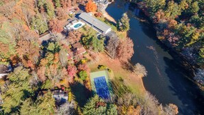 An aerial view of a property with a large house, a tennis court, and a lake.