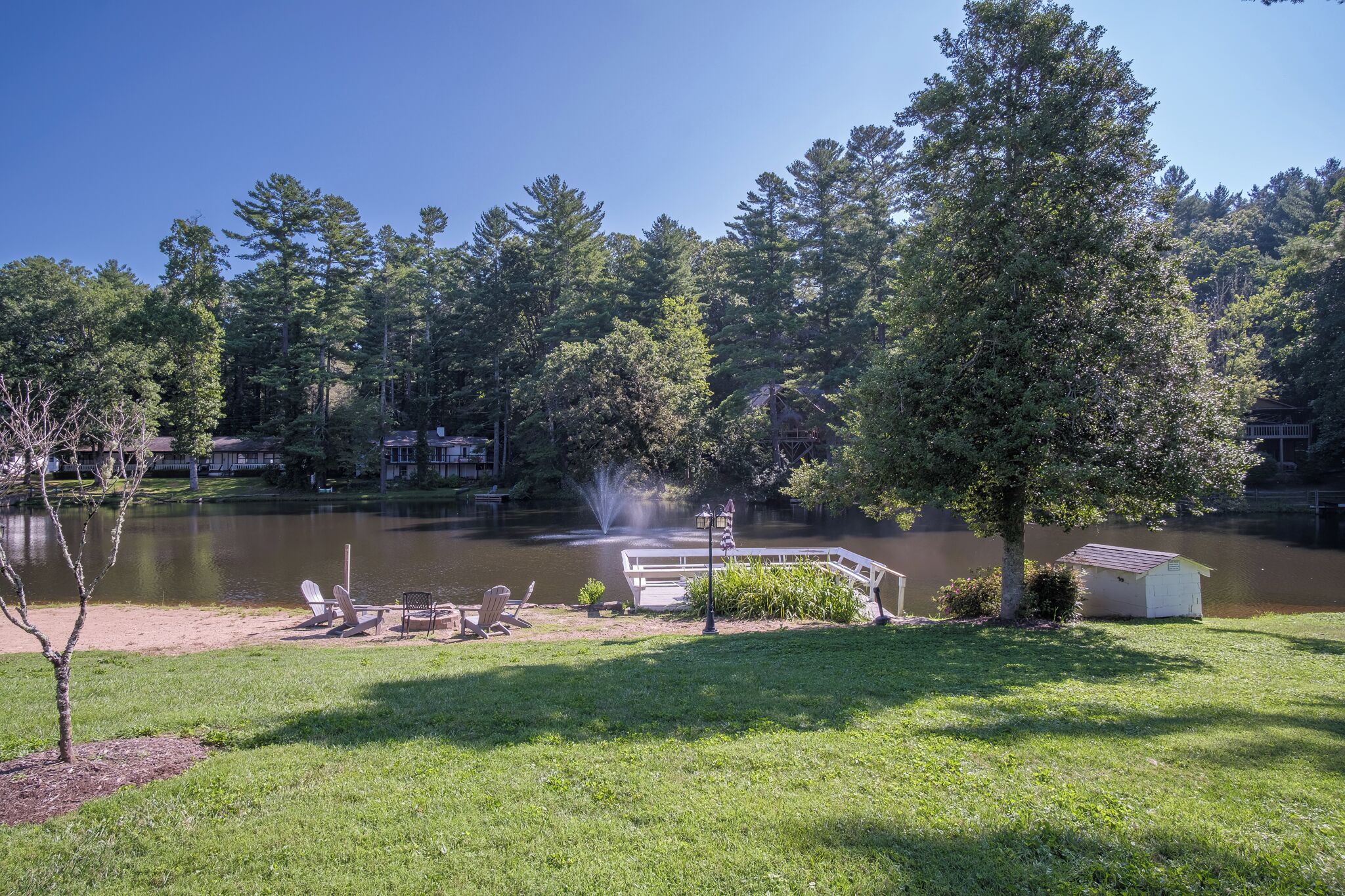 A lakeside park with a dock, chairs, a small shed, and a fountain.