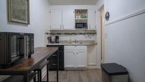 A compact kitchen with white cabinets, a microwave, a coffee maker, and a wooden table.