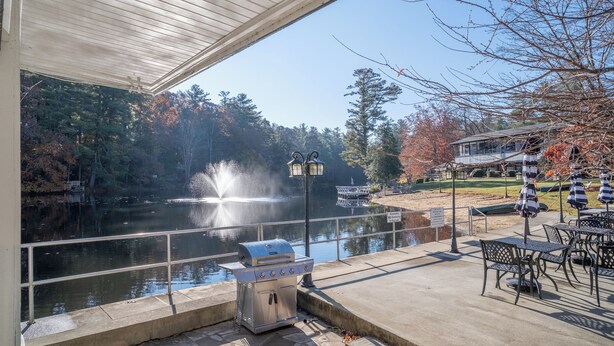 A patio with a grill, outdoor seating, and a view of a lake with a fountain.