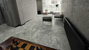 Un intérieur moderne avec un sol en marbre, un jeu d’échecs et une vue sur un chantier de construction, visible à travers une grande fenêtre.