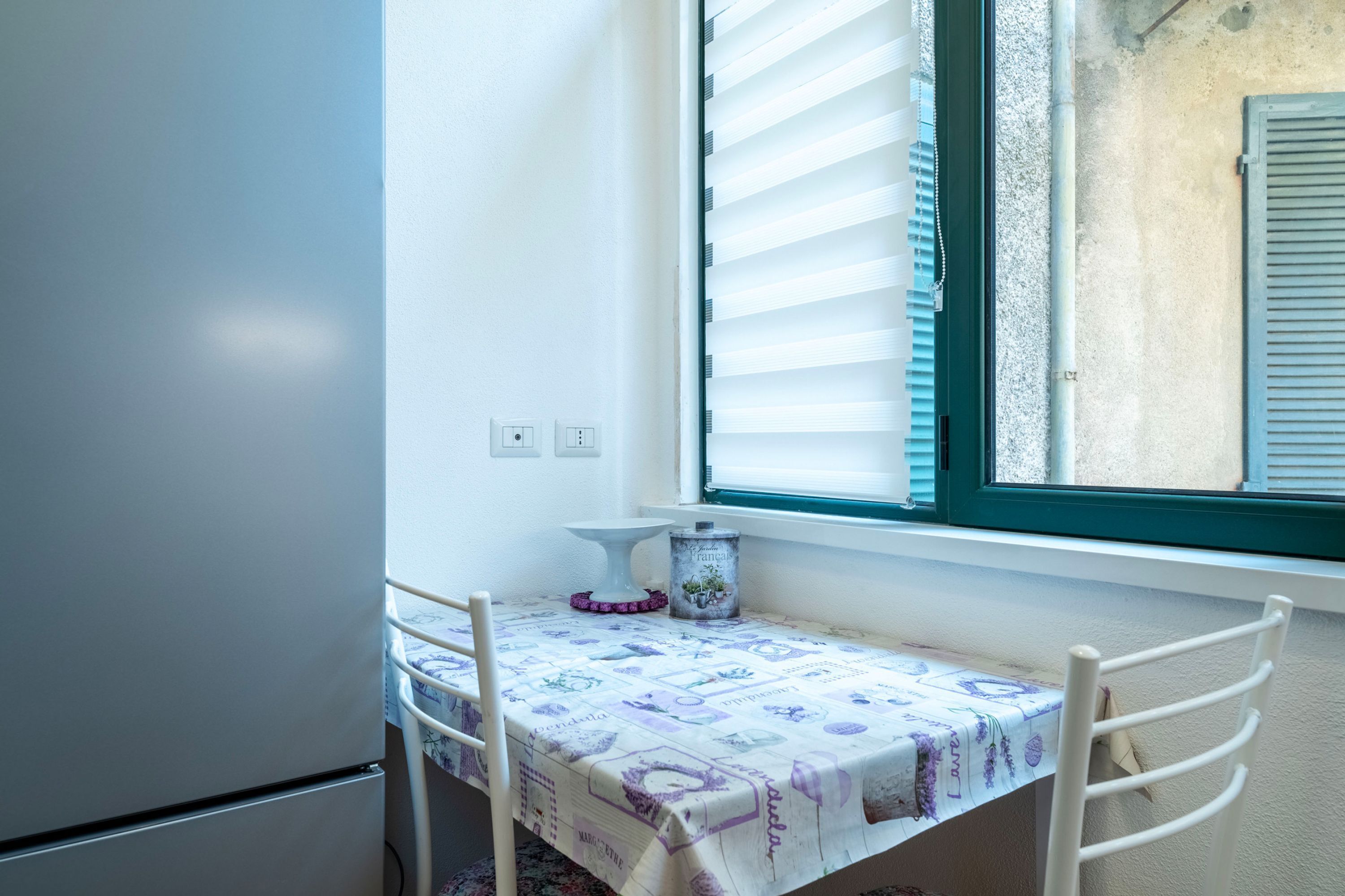 Un pequeño comedor con una mesa cubierta con mantel, una silla y una ventana con persianas.