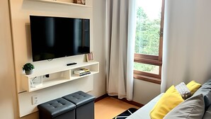 Moderni olohuone, jossa seinälle on asennettu taulutelevisio, on pieni hylly koriste-esineitä varten, penkki ja ikkuna, jossa on verhot.