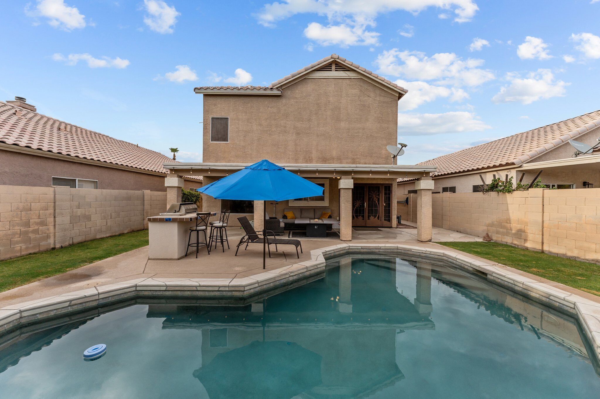 A backyard with a swimming pool, patio furniture, and a house with a tiled roof.