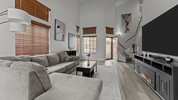 A spacious living room with a large sectional sofa, a fireplace, and a staircase leading to an upper level. - Ultimate Luxury: Home with a Pool and Private Gym! (Tempe)