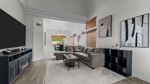 A modern living room with a sectional sofa, a coffee table, and a fireplace. There is a TV mounted on the wall and a bookshelf. - Ultimate Luxury: Home with a Pool and Private Gym! (Tempe)