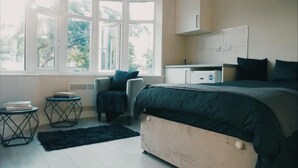 A bedroom with a large bed, a chair, a small table, a radiator, and a window with a view of trees.