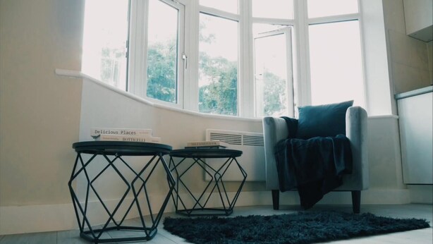 A room with a large window, two small tables with name tags, a chair, and a dark rug.
