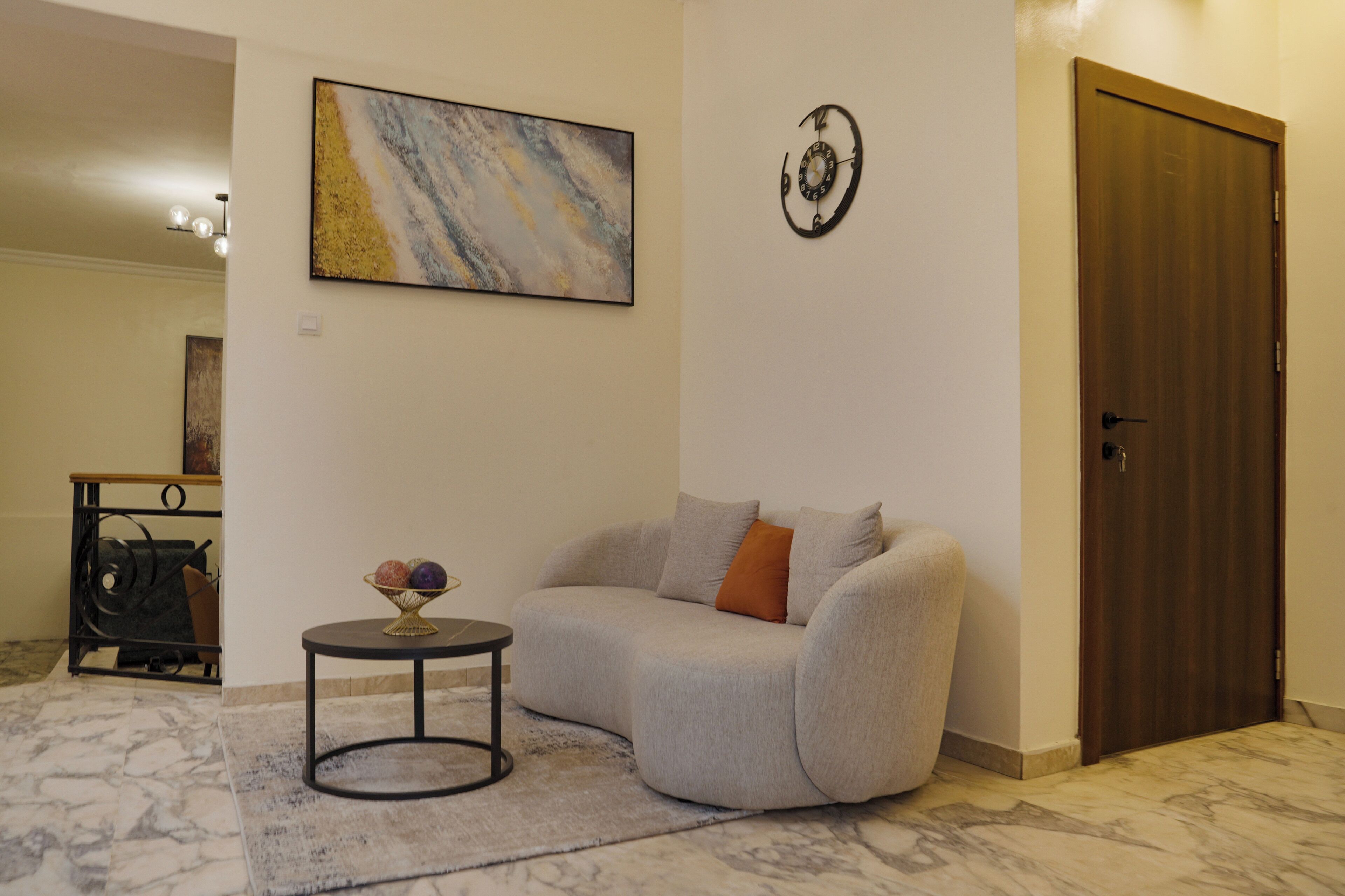 Ein Wohnzimmer mit einer Couch, einem kleinen runden Tisch mit einer Obstschale, einem Bild an der Wand und einer Tür.