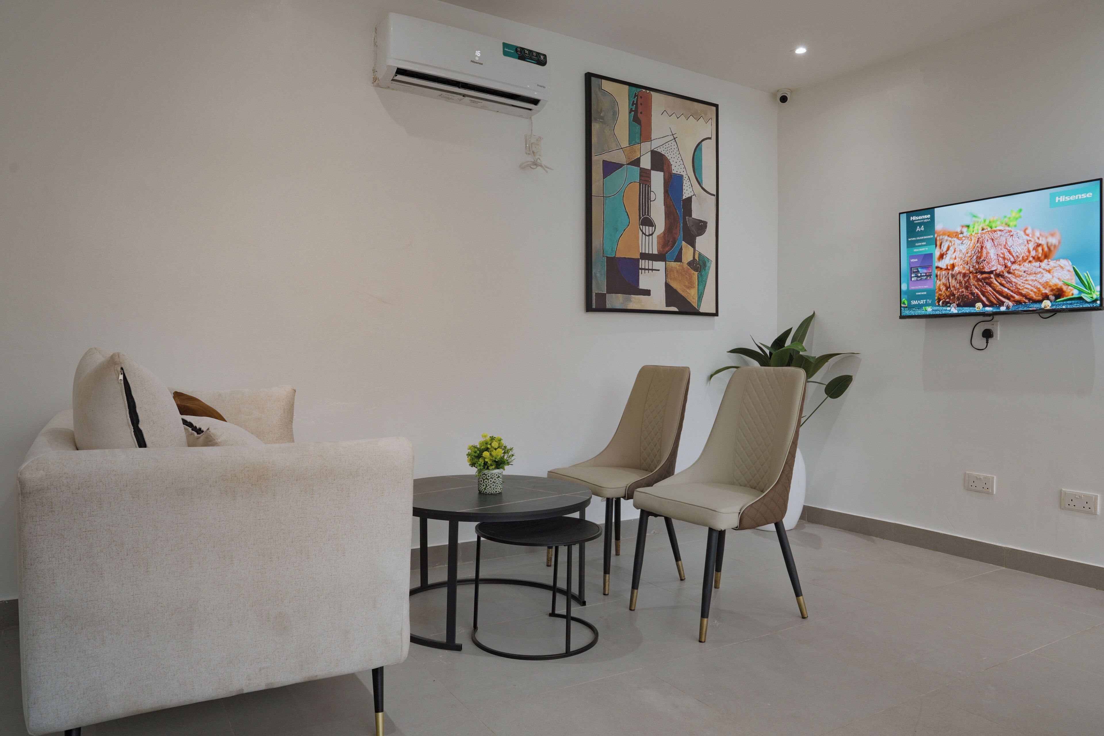 Un salon moderne comprenant un canapé, deux fauteuils, une petite table et un téléviseur à écran plat fixé au mur.