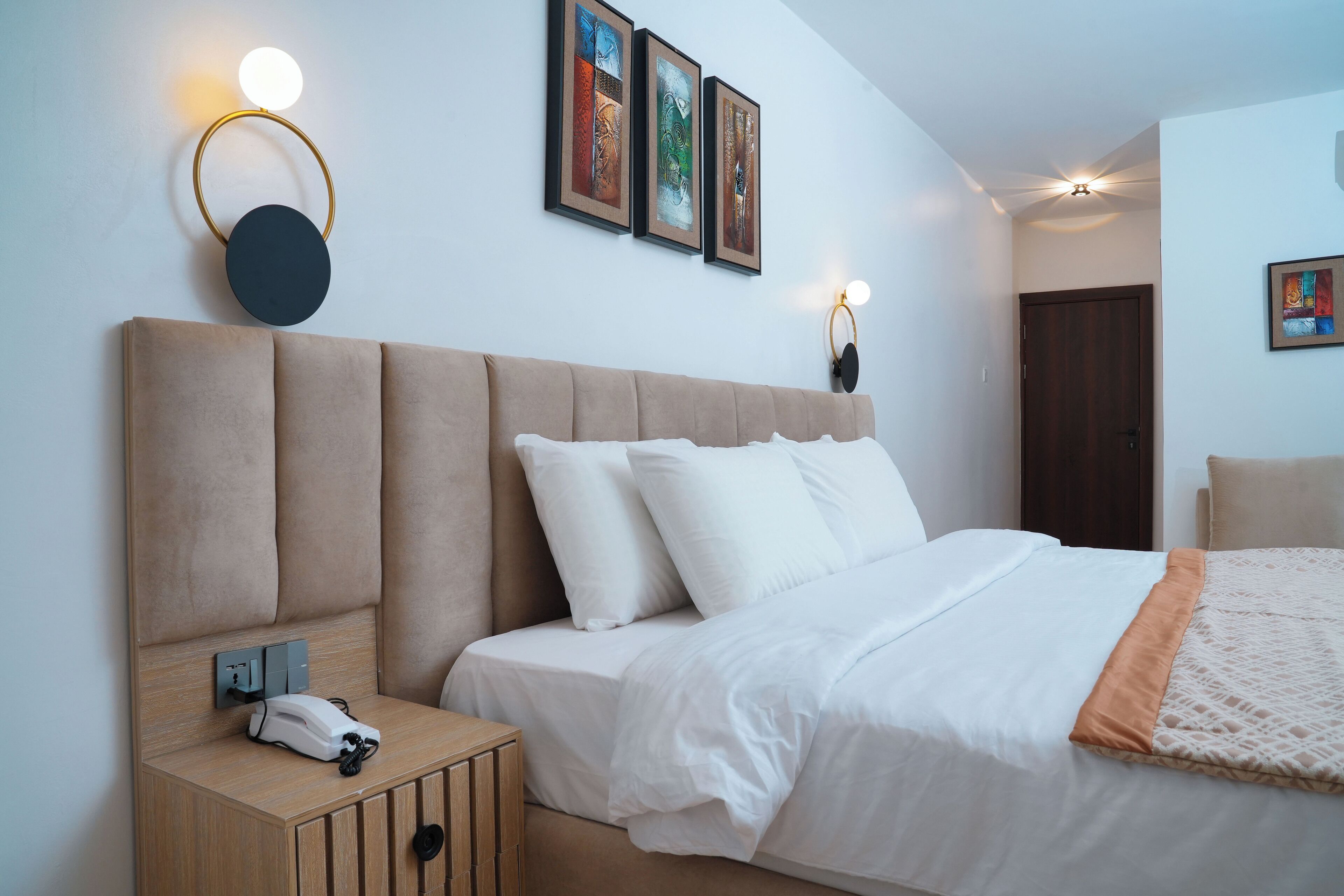 Un dormitorio moderno con una cama grande, una mesita de noche con un teléfono y una obra de arte colgada en la pared.