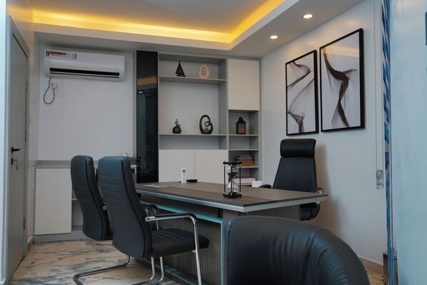 Una oficina moderna con una mesa de vidrio, sillas de cuero negro, una pizarra y estantes con objetos decorativos.