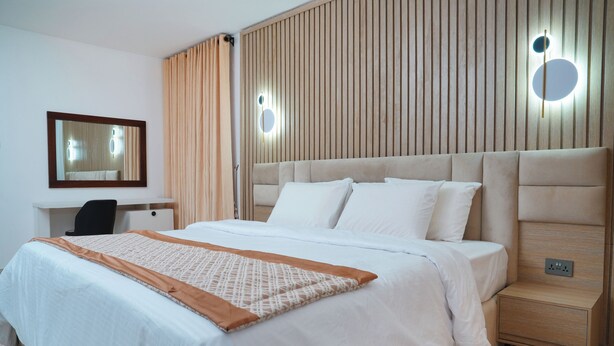 A neatly made bed with a patterned throw, a bedside table with a lamp, and a wall-mounted mirror. - Majestic Courts (Lagos)