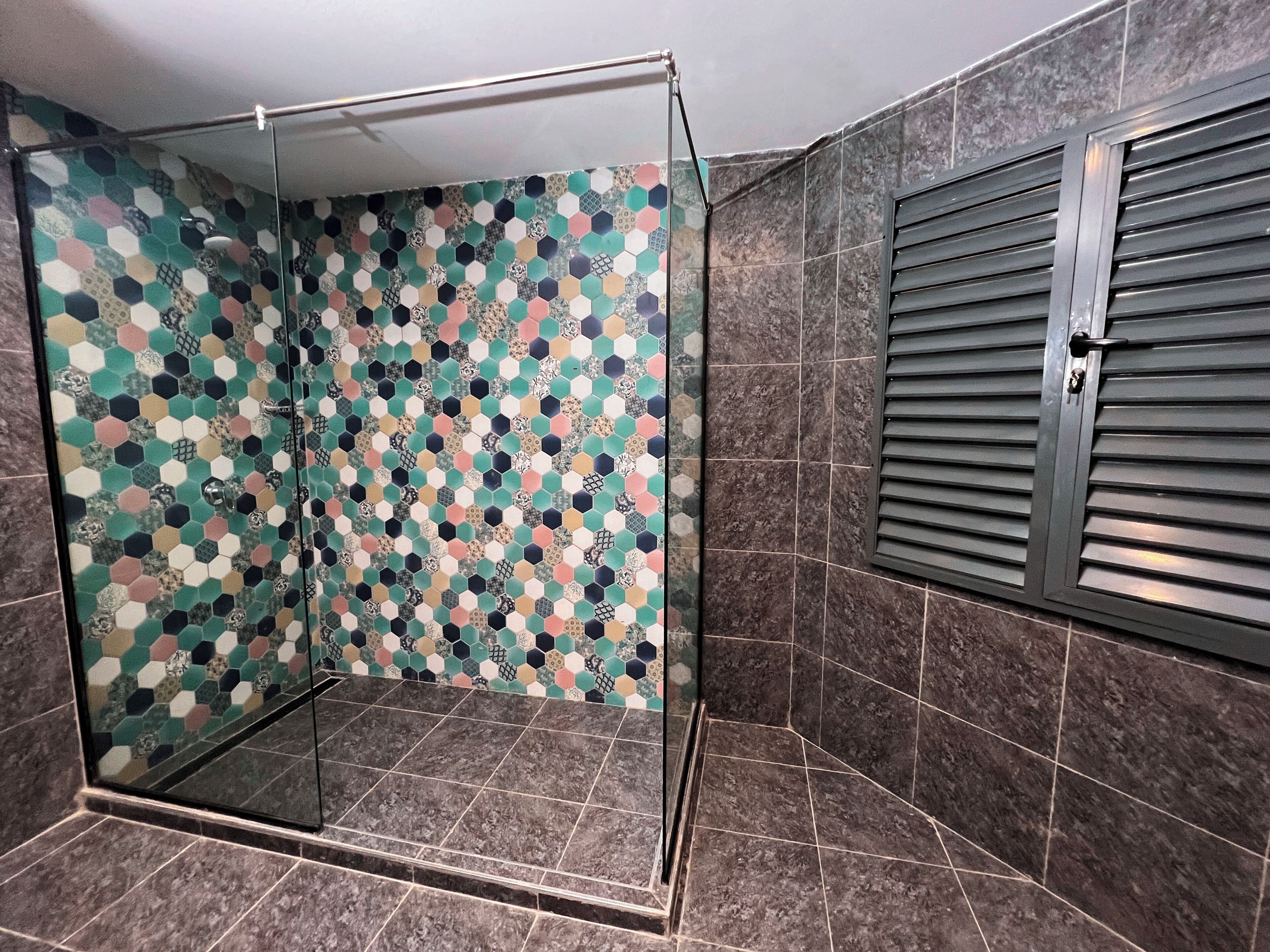 A shower with a glass door and a colorful hexagonal tile pattern on the wall.