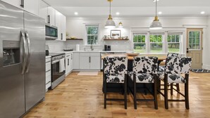 A modern kitchen with stainless steel appliances, a wooden dining table, and black and white patterned chairs.