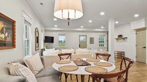 A spacious living room with a round dining table, wooden chairs, and a large chandelier.