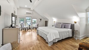 A spacious bedroom with a large bed, a ceiling fan, and a view of the outdoors through the windows.