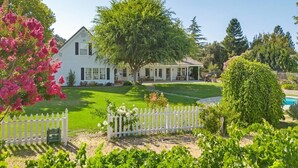 Une maison blanche avec un grand arbre dans le jardin, une clôture blanche en bois et une pelouse bien entretenue.