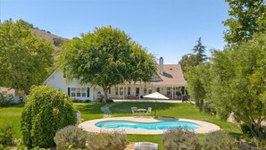 Une maison avec une piscine, entourée d’une pelouse bien entretenue et de diverses plantes.