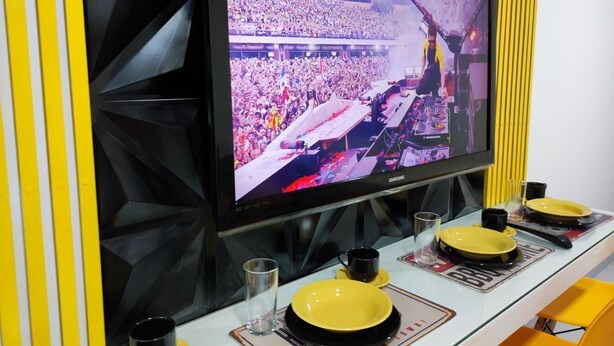Un televisor montado en la pared mostrando un concierto con una multitud numerosa.