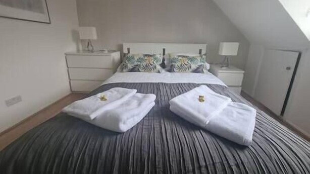 A hotel room with a large bed, two bedside tables, a nightstand, a wall-mounted TV, and a door. - Split level luton town center flat (Luton)