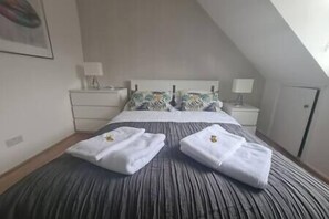 Una habitación de hotel con una cama grande, dos mesitas de noche, un tocador, un televisor montado en la pared y una puerta.
