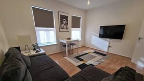 A modern living room with a sofa set, a small dining table, and a TV mounted on the wall. - Split level luton town center flat (Luton)