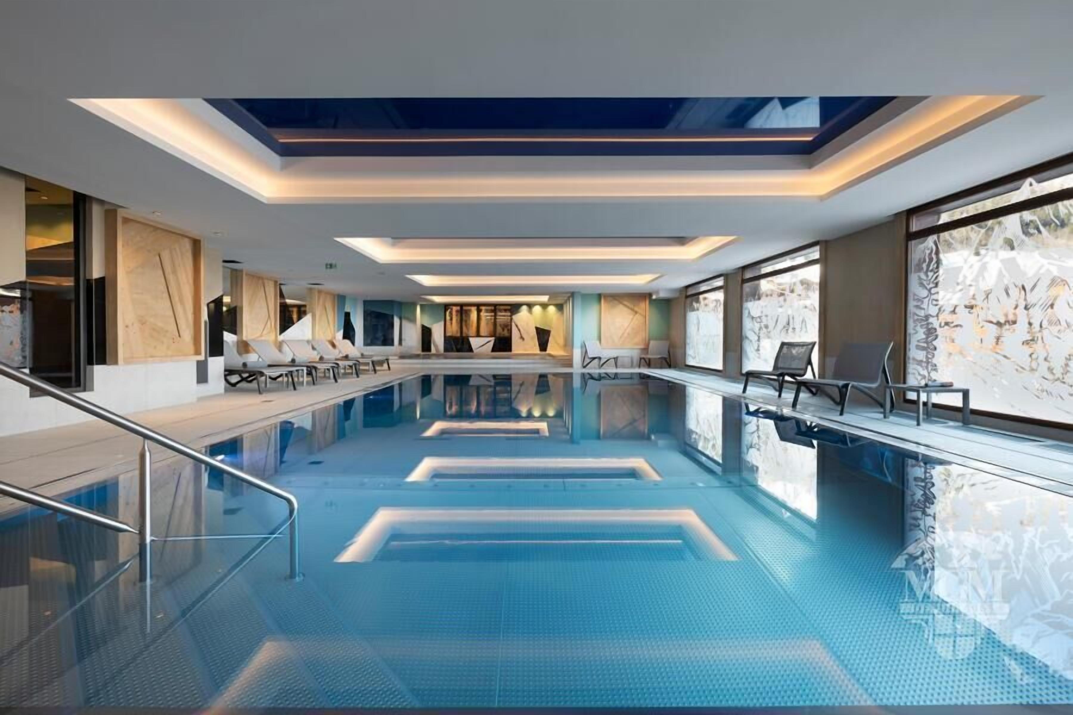 Una piscina interna moderna con acqua cristallina, zone relax a livello e un soffitto con lucernari.