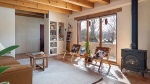 A cozy living room with a fireplace, wooden furniture, and a large window with a view. - Oasis Escondido / Stunning Views / Spa / Firepit / Location / Private! (El Prado)