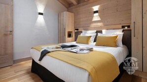 A bedroom with a wooden ceiling, a bed with white bedding and yellow pillows, and a small bedside table. - Wifi, view village, fitness, swimming pool, sauna, hammam, balcony, tv, ski locker, 65m², Valmorel (Valmorel)
