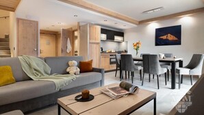 A modern living room with a grey sofa, a coffee table, and a dining area with grey chairs. - Wifi, view village, fitness, swimming pool, sauna, hammam, balcony, tv, ski locker, 65m², Valmorel (Valmorel)