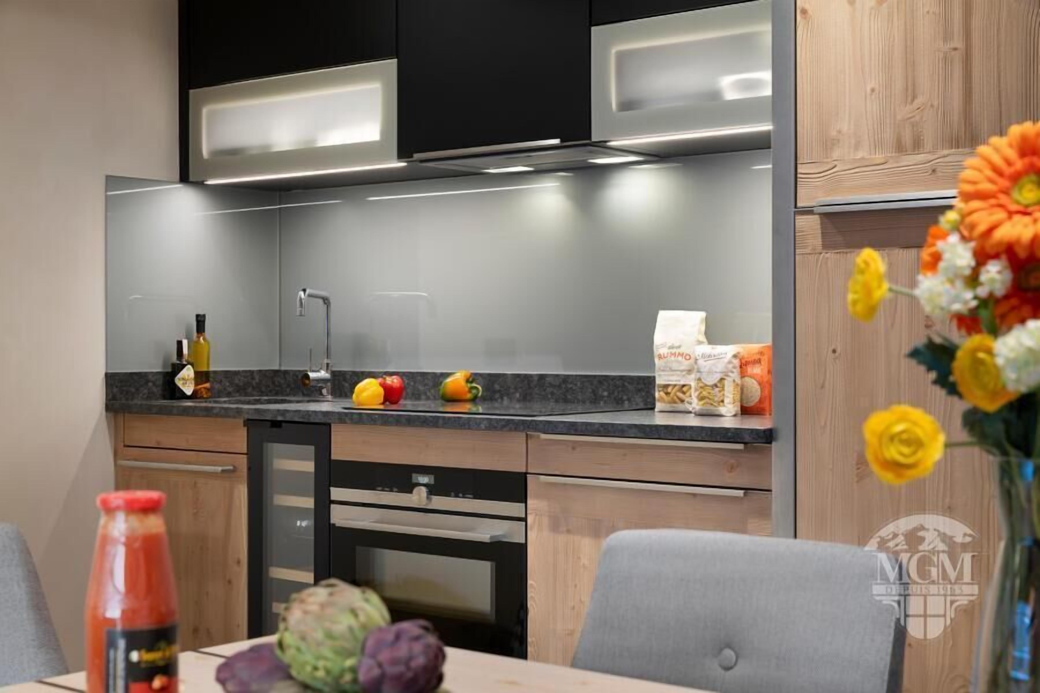 A modern kitchen with a black and grey color scheme, a built-in oven, and a dining area with a table and chairs.