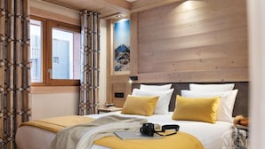 A hotel room with a large bed, wooden panel walls, a window with curtains, and a painting on the wall. - Wifi, view village, fitness, swimming pool, sauna, hammam, balcony, tv, ski locker, 60m², Valmorel (Valmorel)