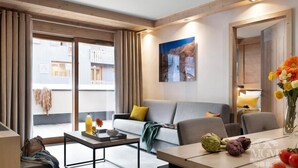 A modern living room with a sofa, coffee table, and a dining area with a vase of flowers and vegetables. - Wifi, view village, fitness, swimming pool, sauna, hammam, balcony, tv, ski locker, 60m², Valmorel (Valmorel)