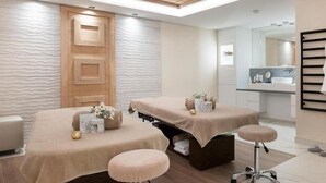 A modern spa room with two massage tables, a wooden ceiling, and a glass shower area.
