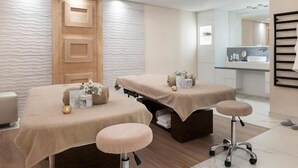 Ein moderner Spa-Raum mit zwei Massagetischen, einer Holzbalkendecke und einem Duschbereich mit Glasabtrennung.