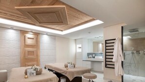Una moderna sala spa con due lettini da massaggio, soffitto in legno e zona doccia in vetro.