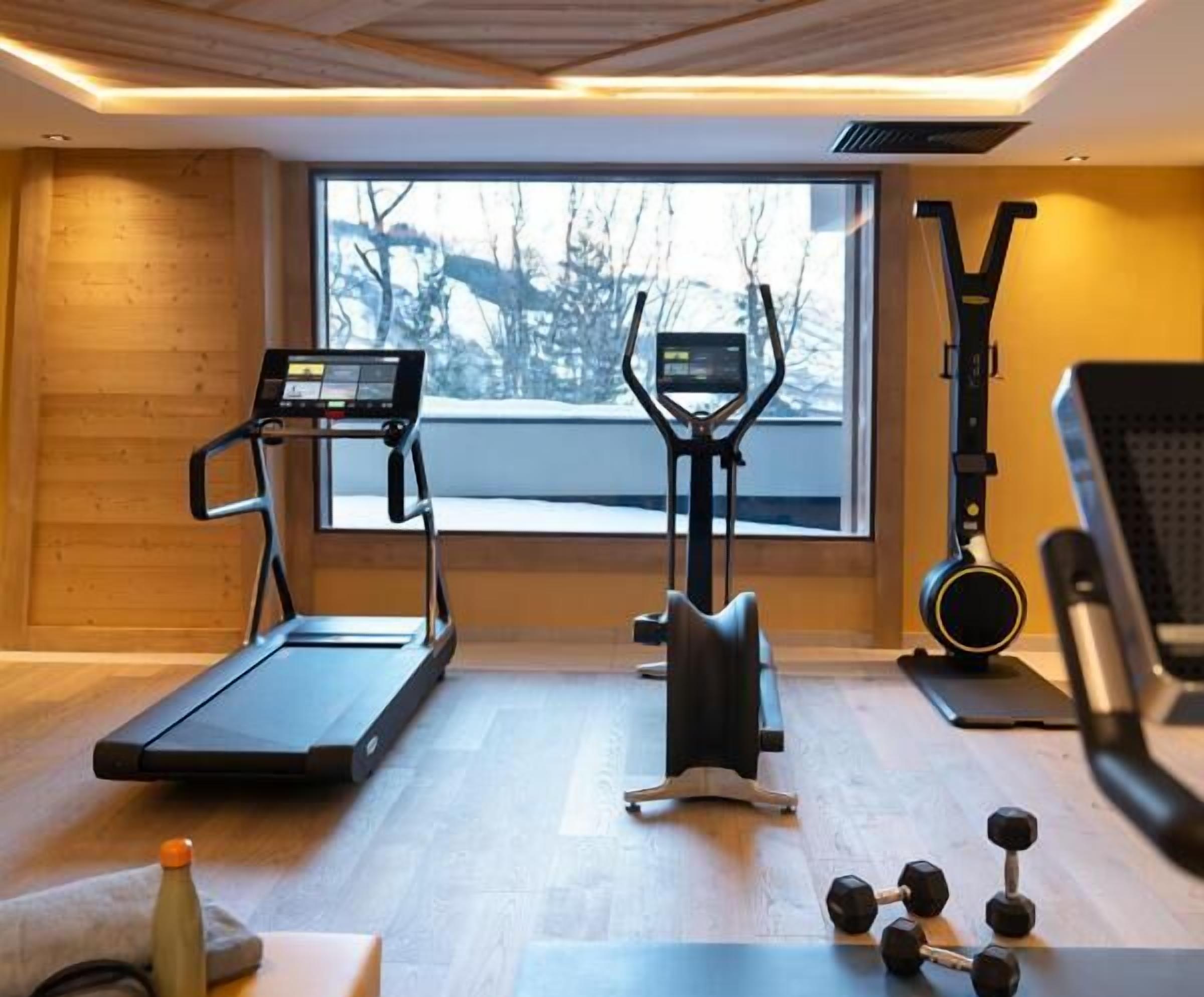 A home gym with a treadmill, elliptical, stationary bike, and dumbbells.