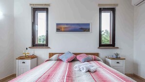 A neatly made bed with a striped bedspread, two bedside tables with lamps and decorative items, and a framed picture on the wall. - Villa La Fata in the country village (Stintino)