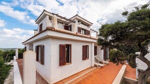 A two-story house with a tiled patio, white walls, and wooden shutters. - Villa La Fata in the country village (Stintino)