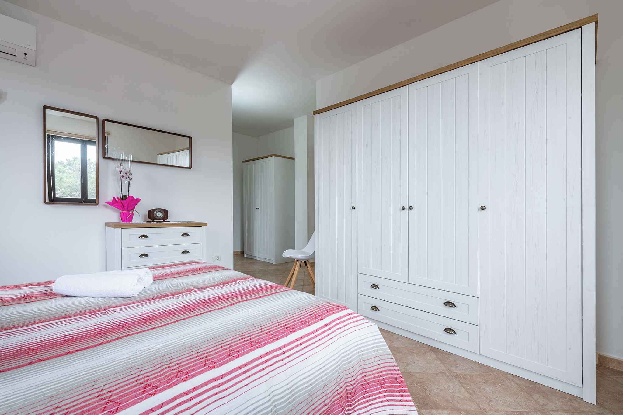 A bedroom with a bed, a wardrobe, a mirror, and a nightstand.
