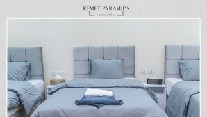 A hotel room with a large bed, two bedside tables, and a bench. There are two pillows on the bed and a tissue box on one of the bedside tables. - Pyramids Lodge (Giza)