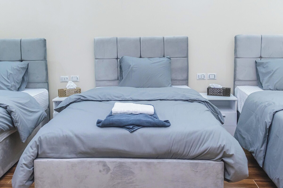 A hotel room with a large bed, two bedside tables, and a bench. There are two pillows on the bed and a tissue box on one of the bedside tables.