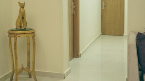 A hallway with a small golden statue on a table, a wooden door at the end, and a couch in the foreground. - Pyramids Lodge (Giza)