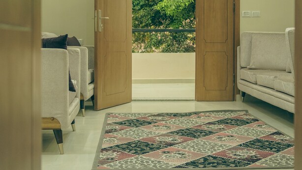 A room with two sofas, a patterned rug, and a wooden door leading to a balcony with greenery. - Pyramids Lodge (Giza)