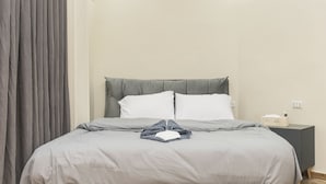 A neatly made bed with a grey headboard and white pillows, a grey blanket, and a folded towel on the bed. - Pyramids Lodge (Giza)